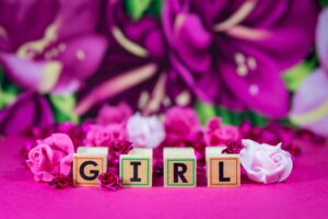 Wooden blocks spelling 'girl' surrounded by pink floral decorations and roses.