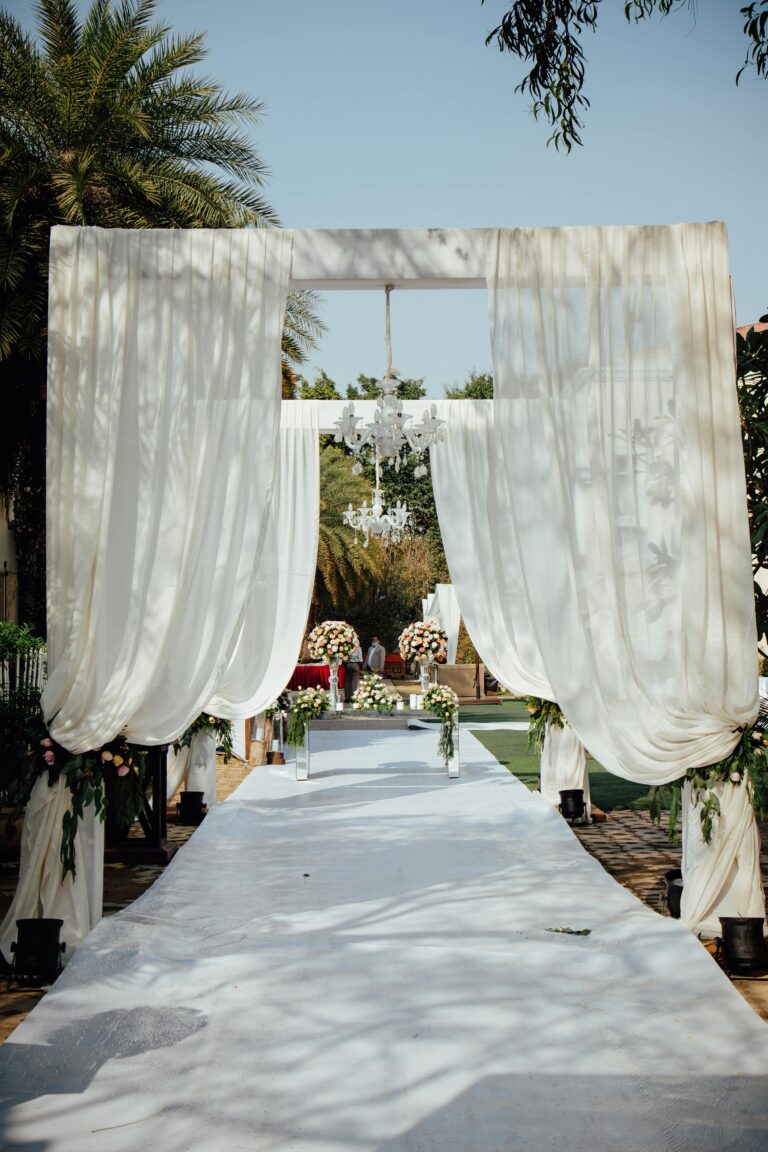 A beautifully decorated outdoor wedding aisle with draped curtains and floral arrangements, set for a ceremony.